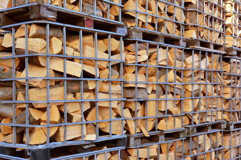 Gestapeltes Brennholz in Metallgitterboxen auf Paletten